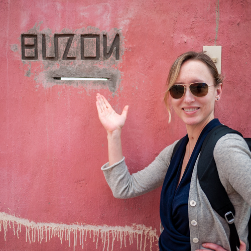 Elisabeth Eaves standing next to a mail slot labeled "buzon," set in a red wall.