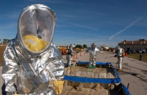 A person in a silver hazmat suit, with others in the background.