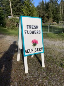 A sandwich board sign that says "Fresh Flowers" with a drawing of a pink flower.